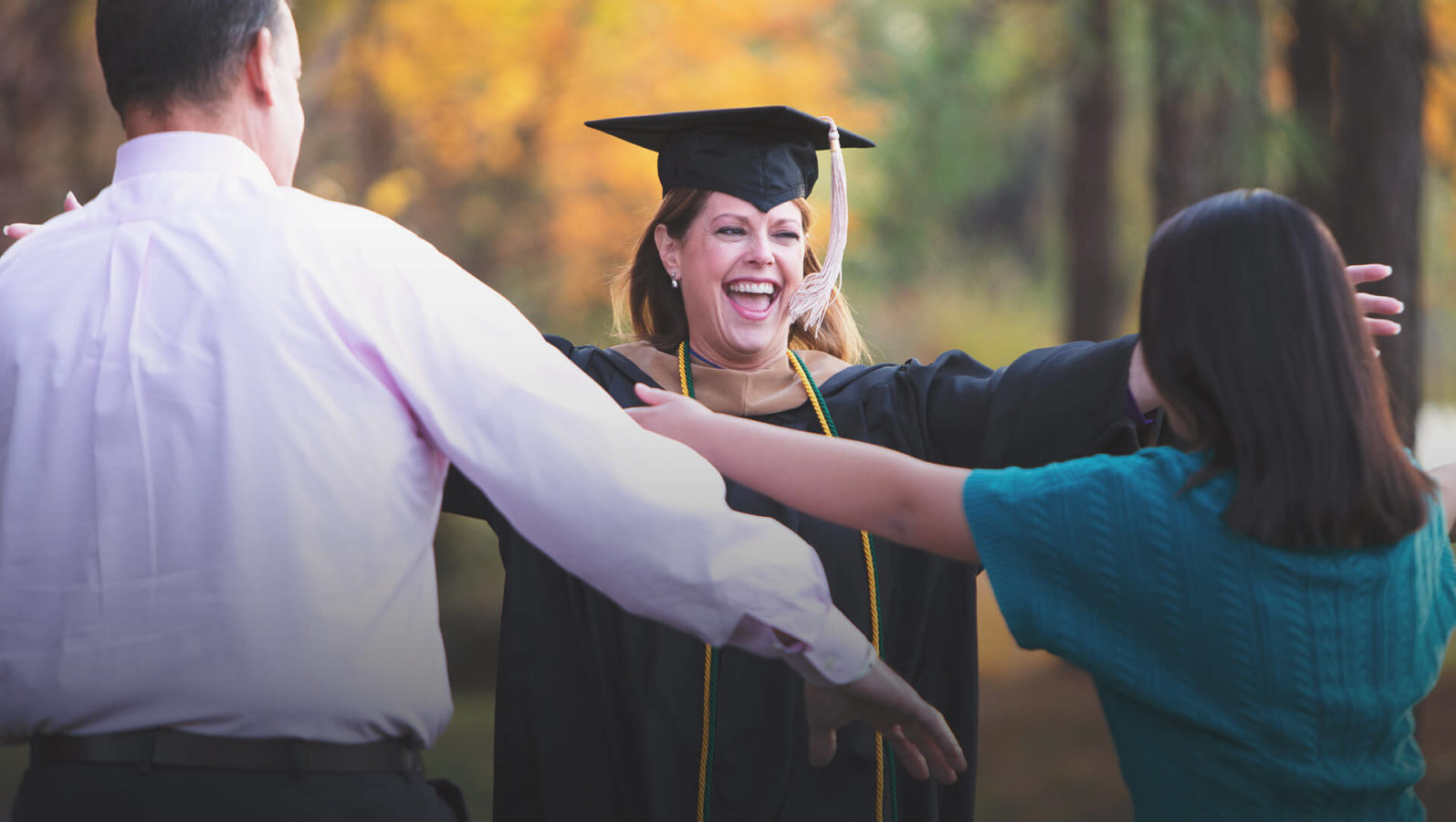 Mom in graduation robe greeting family with open arms