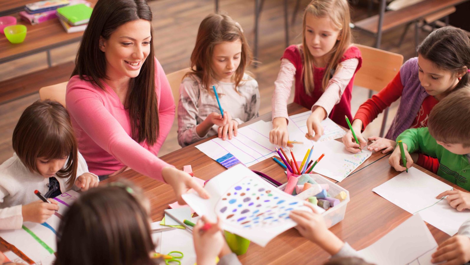 Young teacher sitting at table with children coloring