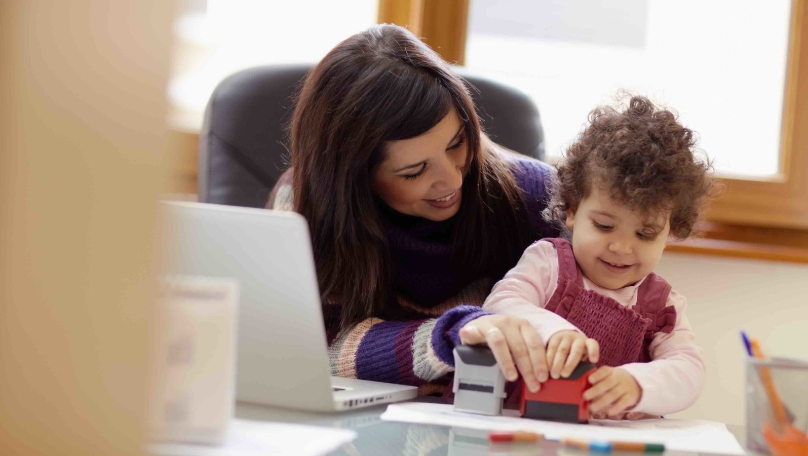 businesswoman working with laptop computer at home and playing with her baby girl. Horizontal shape, front view, waist up