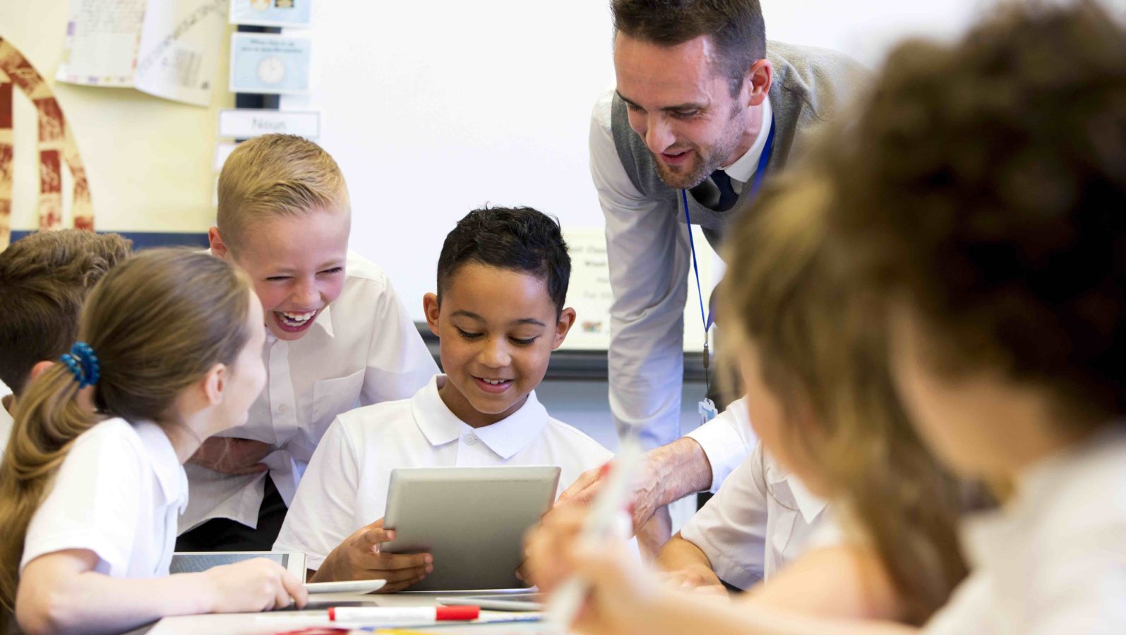 Male teacher supervising a group of children on digital tablets