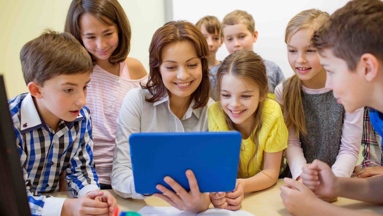 group of school kids with teacher looking to tablet pc computer in classroom